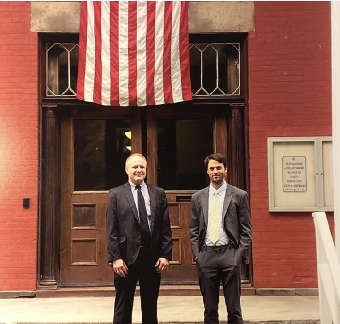 Thomas Plan and Steve Hampsey in suits outside the old Yates County Courthouse, under an American flag.