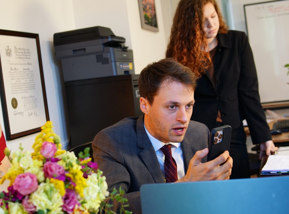 Thomas Plan at his desk on the phone, with his paralegal Leah standing beside him.